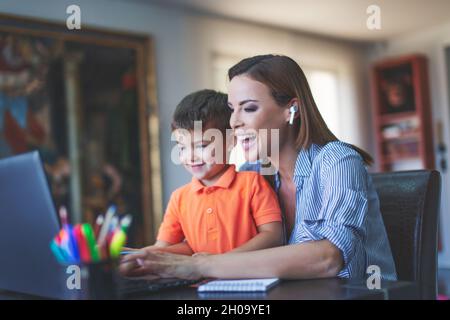 Felice giovane Caucaisan madre e figlio ridendo al portatile in ufficio a casa Foto Stock