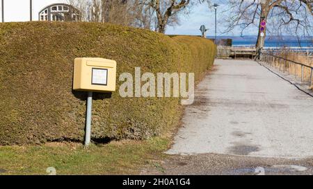 St. Alban, Germania - 2 febbraio 2021: Cassetta postale gialla Deutsche Post di fronte ad un cespuglio verde, oltre ad una piccola strada. Foto Stock