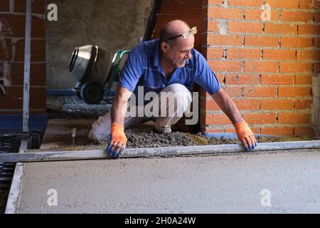 Lavoratori edili che levigano il calcestruzzo al di sopra del sistema di pavimento radiante. Foto Stock