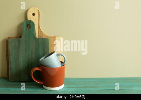 Tazza e vassoio di legno, tagliere su tavola di legno verde. Parete di fondo kaki. Interno cucina Foto Stock