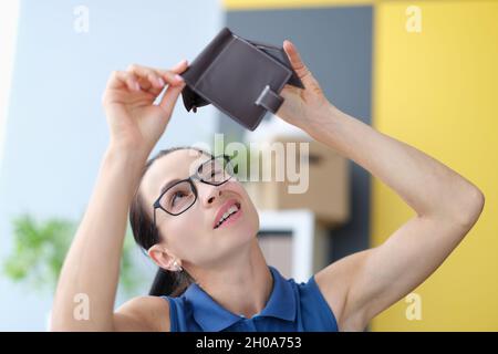 Giovane donna con occhiali che guarda in un portafoglio vuoto in pelle Foto Stock