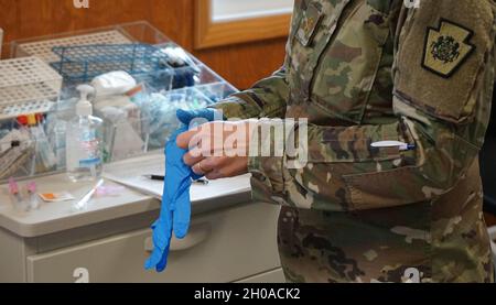 Maja Michelle Nyameke, un'infermiera registrata con il distacco medico della Guardia Nazionale della Pennsylvania, indossa un paio di guanti in preparazione alla somministrazione di una dose di vaccino COVID-19 al prossimo soldato durante le vaccinazioni l'8 gennaio 2021, a Fort Indiantown Gap, Pa. Soldati e Airmen sono stati sottoposti a screening e i loro record aggiornati per proteggere tutti i membri del servizio coinvolti nel processo di vaccinazione. Foto Stock