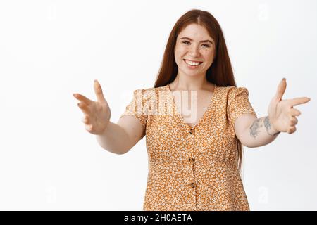 Ragazza curvilinea tenera e femminile che stende le mani per abbracciare, cordiale benvenuto con abbracci, in piedi su sfondo bianco Foto Stock