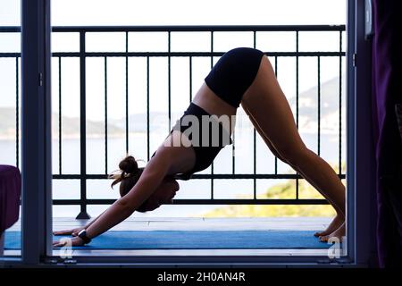 Giovane donna fitness che fa pratica di yoga al mattino sul balcone vicino al mare Foto Stock