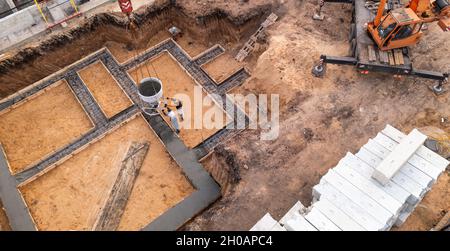 Cantiere con operai che versano calcestruzzo in casseforme con rinforzo. Il cemento bagnato si riversa sulla fondazione dell'edificio civile, vista aerea. Foto Stock