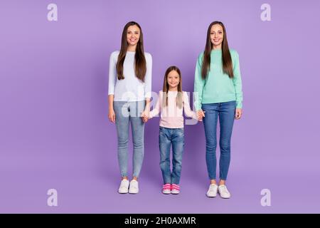 Foto di dolce divertente mummia due figlie indossare pullover casual tenendo le mani camminare sorridendo isolato viola sfondo di colore Foto Stock