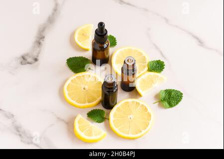 bottiglie cosmetiche di vetro scuro con oli essenziali di limone e foglie di balsamo al limone su un tavolo di marmo Foto Stock