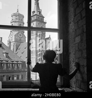 Eien Frau blickt durch ein Fenster auf die Stiftskirche am Schillerplatz in Stoccarda, Deutschland 1930er Jahre. Una donna di guardare attraverso una finestra la chiesa collegiata a Schillerplatz square a Stuttgart, Germania 1930s. Foto Stock