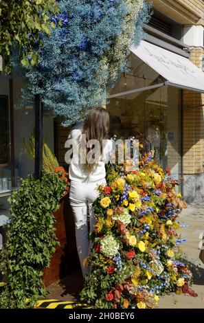 Giovane donna che regola un display floreale durante Chelsea in Bloom annuale mostra d'arte floreale e doccia di fiori nei negozi e le strade di Chelsea messo sopra Foto Stock