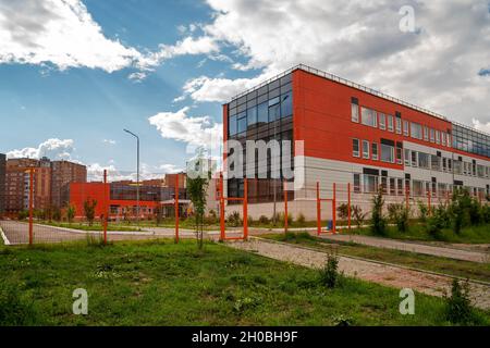 Edificio moderno di una scuola superiore comunale completa con lezioni gratuite dietro la recinzione in una zona residenziale in estate. Foto Stock