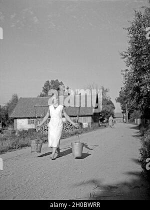 Eine Frau trägt Wasser über die Dorfstraße von Elchwerder Memeldelta im in Ostpreußen, 1930er Jahre. Una donna che porta acqua al villaggio principale strada di Elchwerder nel Memel delta, Prussia orientale, 1930s. Foto Stock