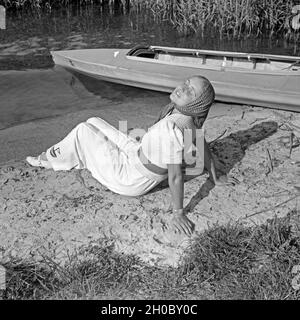 Eine junge Frau beim Sonnenbad am Ufer eines vede, neben einem Klepper Faltboot Typ T6, Deutschland 1930er Jahre. Una donna a prendere il sole sulla riva di un lago con una piegatura Klepper barca, Germania 1930s. Foto Stock