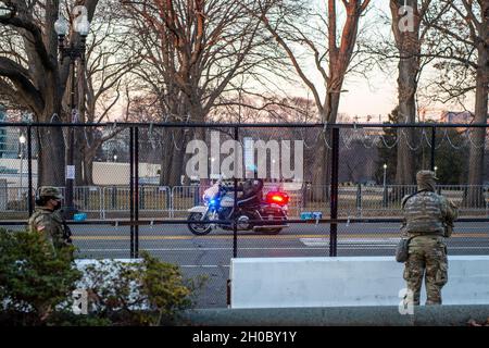 Soldati degli Stati Uniti con la guardia nazionale dell'Oklahoma, come ufficiale della polizia del Campidoglio degli Stati Uniti guida su una motocicletta vicino al Campidoglio degli Stati Uniti a Washington, D.C., 20 gennaio 2021. Almeno 25,000 uomini e donne della Guardia Nazionale sono stati autorizzati a condurre missioni di sicurezza, comunicazione e logistica a sostegno delle autorità federali e distrettuali che hanno condotto fino alla 59a Inaugurazione Presidenziale e che hanno attraversato la stessa. Foto Stock