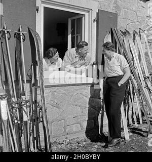 Skifahrer unterhalten sich durchs Fenster einer Skihütte, Deutschland 1930er Jahre. Gli sciatori in chat al di fuori della finestra di un rifugio sciistico, Germania 1930s. Foto Stock