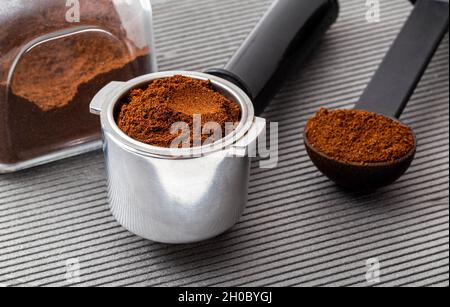 Un vasetto di caffè, il corno di una macchina da caffè e un misurino su sfondo grigio. Foto Stock