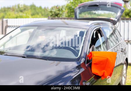 Un giubbotto di segnalazione arancione è appeso allo specchio di un'autovettura. Concetto di guasto dell'auto, segnale di assistenza stradale, problemi Foto Stock