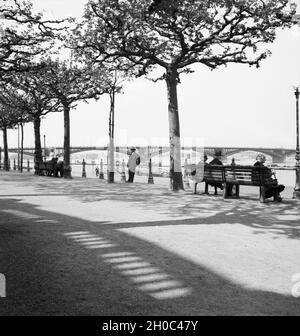 Mainzer sitzen am Rheinufer in Mainz und schauen auf den Rhein und die Straßenbrücke, Deutschland 1930er Jahre. La gente seduta sulle rive del fiume Reno a Mainz, Germania 1930s. Foto Stock