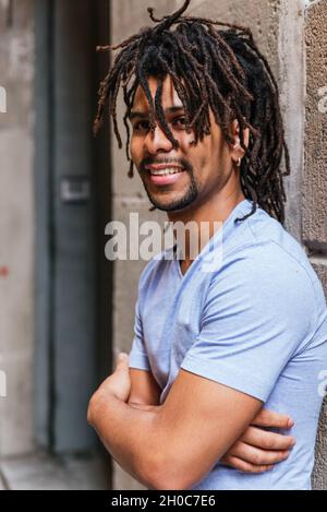 ritratto verticale di un giovane ispanico con i dreadlocks. Sta guardando la macchina fotografica e sorride Foto Stock