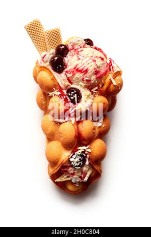 Vista dall'alto del gustoso cono di waffle all'uovo riempito con bacche in gelato con sciroppo e cioccolato bianco su sfondo bianco Foto Stock