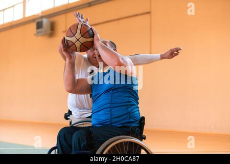 I veterani della guerra disabili hanno mescolato le squadre di pallacanestro di età e di corsa in carrozzina che giocano un match di addestramento in una sala della palestra di sport. Disabili Foto Stock