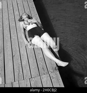 Eine junge Frau beim sonnenbaden auf einem Holzsteg un einem vedere, Deutschland 1930er Jahre. Una giovane donna sdraiata su una passerella sulla riva di un lago, Germania 1930s. Foto Stock