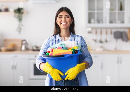 Giovane casalinga che tiene secchio con gli attrezzi di rifornimento di pulizia in cucina Foto Stock