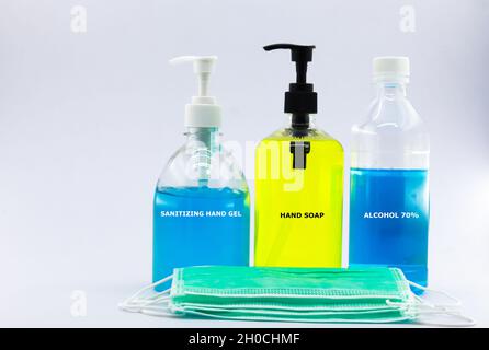 Gel igienizzante blu, sapone liquido, alcool al 70% e molte maschere facciali davanti a loro. Sfondo bianco, spazio di copia. Foto Stock