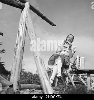 Eine junge Frau sitzt Mit einem Akkordeon un einem Zaun, Deutschland 1930er Jahre. Una giovane donna seduta da un recinto con una fisarmonica Germania 1930s. Foto Stock