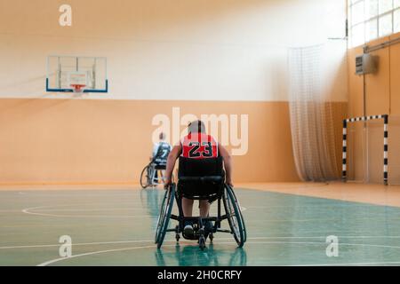 il ragazzo si siede su una sedia a rotelle e si prepara per l'inizio del gioco di basket nella grande arena Foto Stock