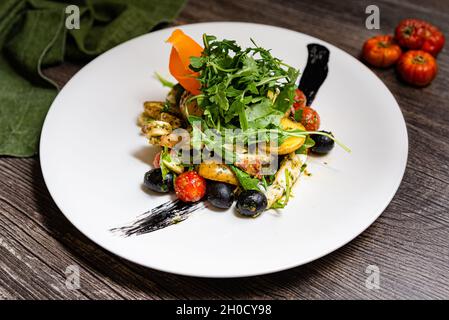 Insalata italiana con polpo in stile ligure. Rucola, olive nere, pomodori ciliegini, tentacoli di polpo, fette di patate novelle, inchiostro seppie. Su un da Foto Stock