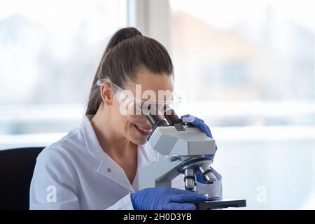 Giovane bella donna che guarda attraverso il microscopio in laboratorio Foto Stock