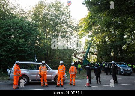 Wendover, Regno Unito. 10 ottobre 2021. Una mongolfiera passa sopra gli agenti di applicazione del National Eviction Team (NET) e gli ufficiali della polizia della Thames Valley che prendono parte al primo giorno di un'operazione per sottrarsi agli attivisti ambientali opposti al collegamento ferroviario ad alta velocità HS2 dal campo di resistenza attiva (GUERRA) di Wendover. IL campo DI GUERRA, che contiene case di alberi, gallerie, una gabbia e una torre di 15 metri, è attualmente il più grande dei campi di protesta allestiti dagli attivisti della Stop HS2 lungo la fase 1 dell'HS2 tra Londra e Birmingham. Credit: Mark Kerrison/Alamy Live News Foto Stock