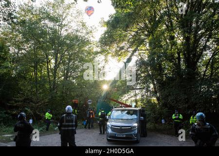 Wendover, Regno Unito. 10 ottobre 2021. Una mongolfiera passa sopra gli agenti di applicazione del National Eviction Team (NET) e gli ufficiali della polizia della Thames Valley che prendono parte al primo giorno di un'operazione per sottrarsi agli attivisti ambientali opposti al collegamento ferroviario ad alta velocità HS2 dal campo di resistenza attiva (GUERRA) di Wendover. IL campo DI GUERRA, che contiene case di alberi, gallerie, una gabbia e una torre di 15 metri, è attualmente il più grande dei campi di protesta allestiti dagli attivisti della Stop HS2 lungo la fase 1 dell'HS2 tra Londra e Birmingham. Credit: Mark Kerrison/Alamy Live News Foto Stock