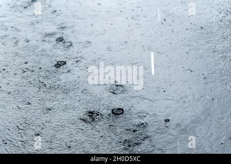 Gocce di pioggia che cadono sull'acqua in una pozzanghera sulla strada. Messa a fuoco selettiva Foto Stock