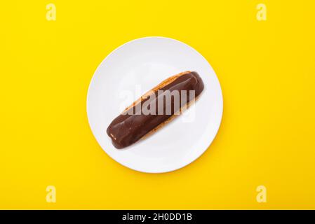 Eclair al cioccolato sul piatto di ceramica con superficie giallo brillante. Composizione minima. Vista dall'alto. Foto Stock