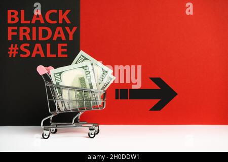 Carrello pieno di soldi per lo shopping del venerdì nero su sfondo colorato con l'iscrizione. Foto Stock