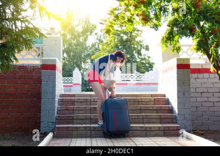 Una donna con valigia pesante difficilmente sale le scale della stazione ferroviaria. Foto Stock