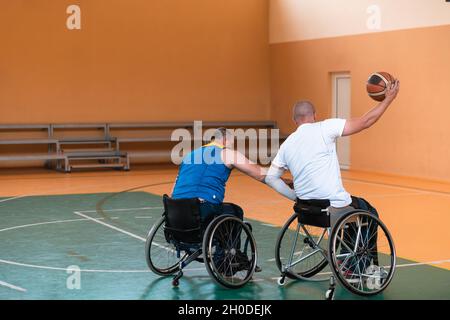 I veterani della guerra disabili hanno mescolato le squadre di pallacanestro di età e di corsa in carrozzina che giocano un match di addestramento in una sala della palestra di sport. Disabili Foto Stock