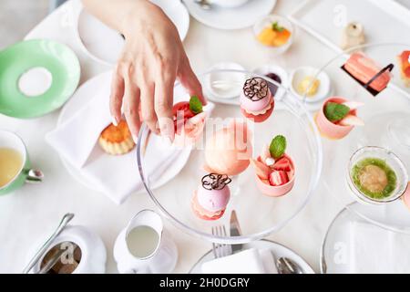 vista ad angolo alto della mano di donna asiatica che raccoglie un dessert da un piatto di vetro sul tavolo Foto Stock