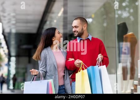 Ritratto di sorridente giovane coppia interrazziale con borse shopping che si guardano l'un l'altro al centro commerciale Foto Stock