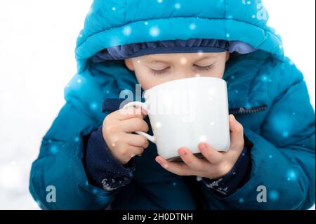 Ragazzino che beve cioccolata calda in una giornata nevosa Foto Stock