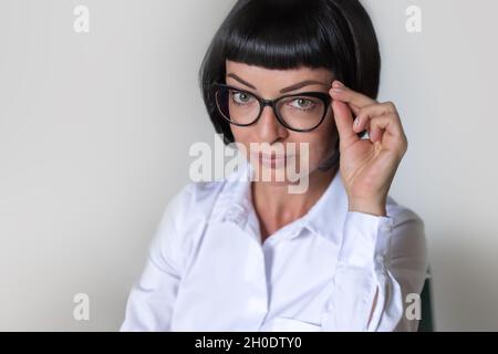 Ritratto di una donna di mezza età con capelli scuri, in una camicia bianca con occhiali. Su sfondo bianco Foto Stock