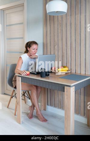 Giovane donna che lavora su un computer e che tiene una mela Foto Stock