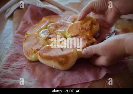 Le mani delle donne ripartiscono le torte calde della rosia cotte con le prugne su un vecchio straccio sul tavolo Foto Stock