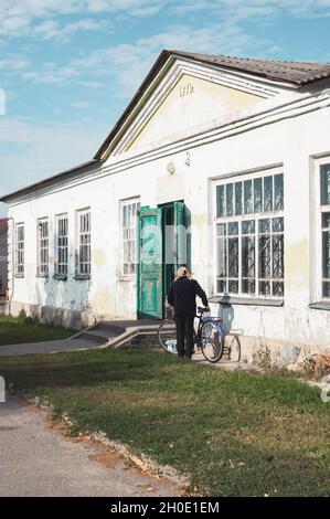 Una donna si mette in bicicletta accanto ad un vecchio edificio vintage peeling del 1971 Foto Stock