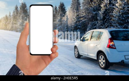 Mano con un telefono sullo sfondo di una macchina dietro una strada invernale. Schermata vuota, è possibile aggiungere il contenuto Foto Stock