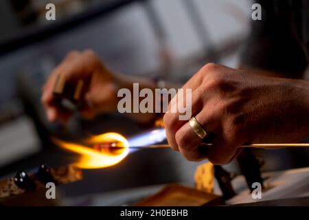 Le mani di un lavoratore di fiamma durante la fabbricazione di perle di vetro. Questa arte è stata iscritta nel 2020 sulla lista rappresentativa del patrimonio culturale immateriale Foto Stock