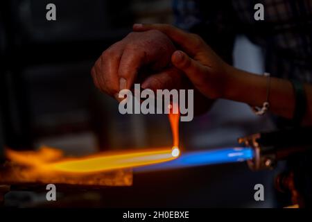 La mano di un lavoratore di fiamma e la mano di un bambino durante la fabbricazione di perle di vetro. Questa arte è stata inscritta nel 2020 sulla lista rappresentativa dell'intangibile Foto Stock