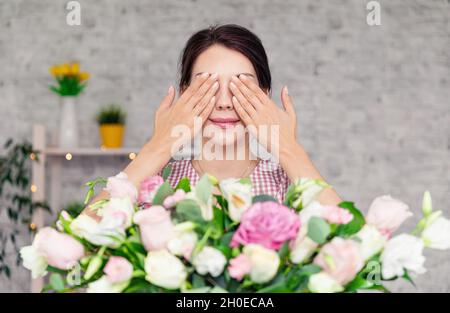 Giovane ragazza con occhi chiusi riceve bouquet di fiori. La donna riceve un regalo di compleanno. Ragazza felice che tiene bouquet di rose Foto Stock