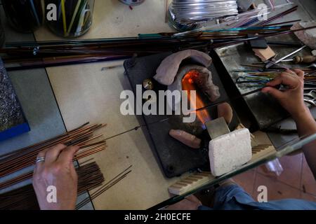 Le mani di un lavoratore di fiamma durante la fabbricazione di perle di vetro. Questa arte è stata iscritta nel 2020 sulla lista rappresentativa del patrimonio culturale immateriale Foto Stock